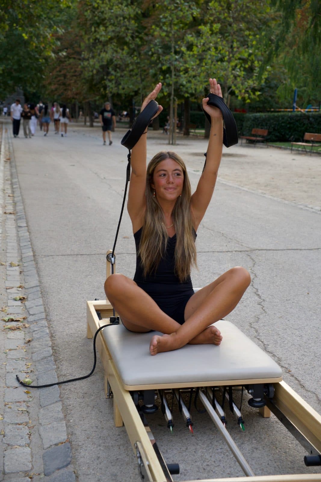 Alumna sentada en el reformer con los brazos en alto sujetando las correas